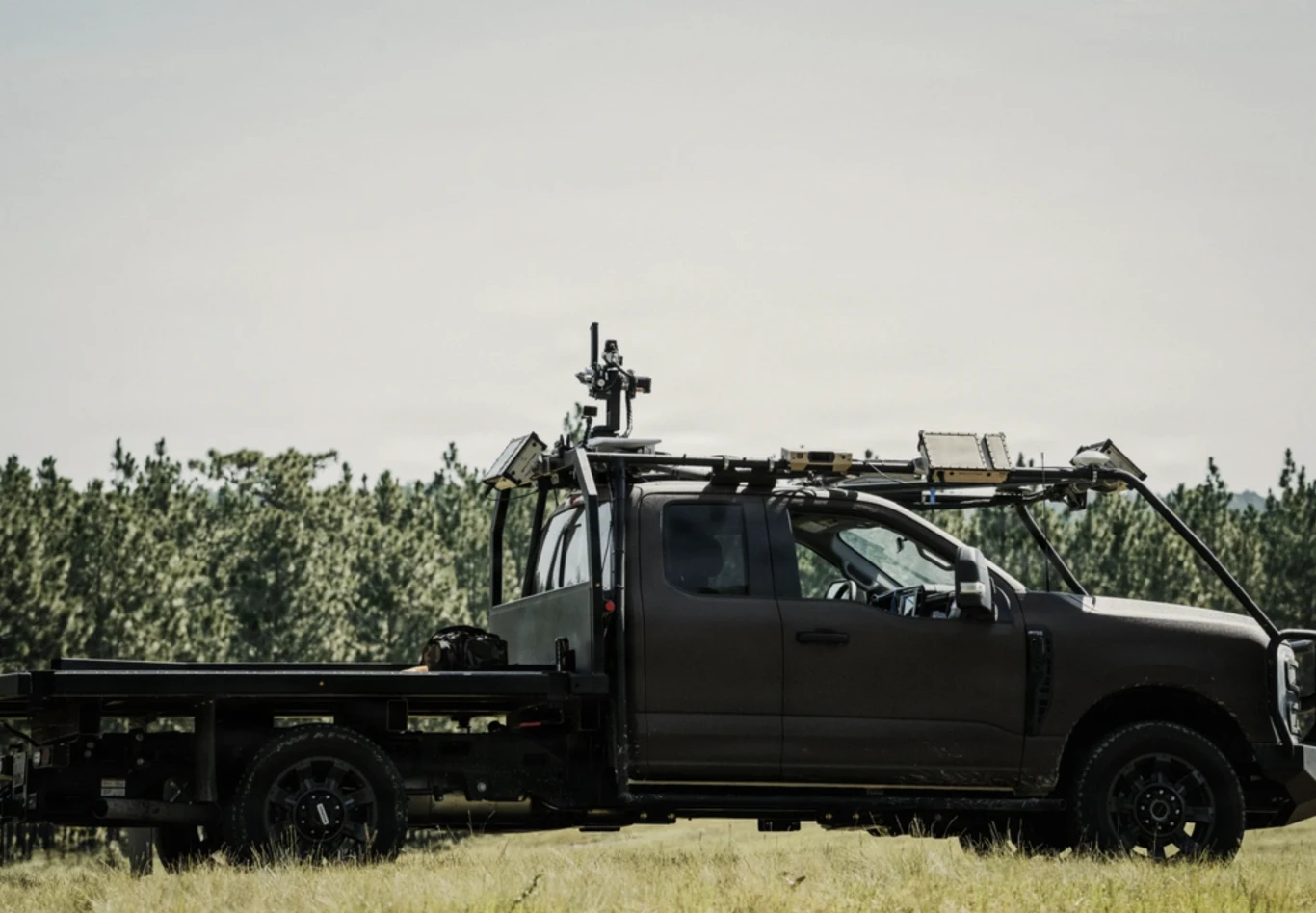 Amerykańska armia coraz chętniej eksperymentuje z autonomicznymi pojazdami, jak ten Ford F-250 Czarny autonomiczny Ford F-250 z systemem antydronowym na dachu, na polu przy drzewach.