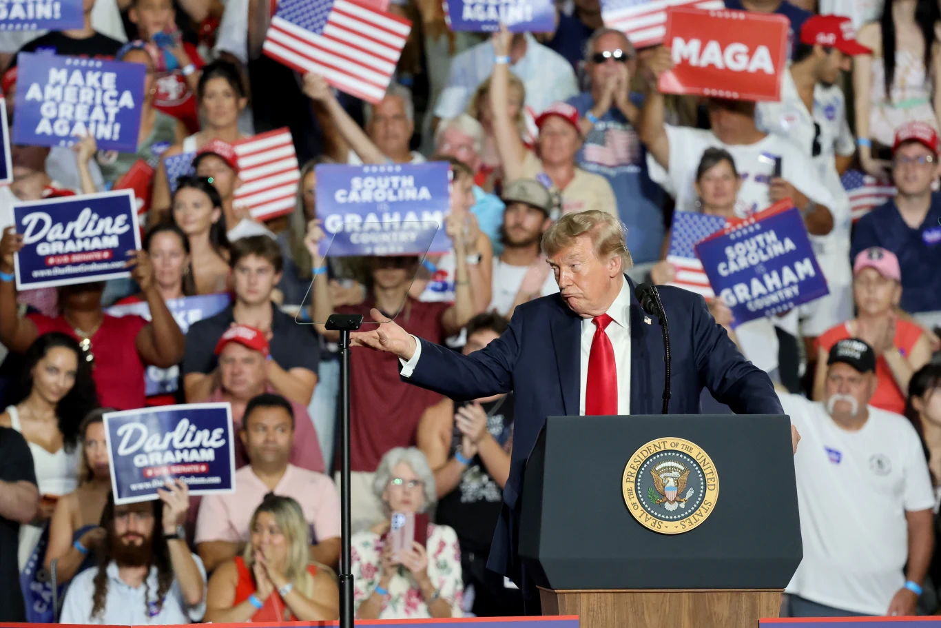 Donald Trump przemawiał w piątek w Myrtle Beach na wiecu poparcia dla Darline Graham Donald Trump stoi za mównicą z prezydenckim herbem, zwrócony bokiem do tłumu, wśród zgromadzenia osób trzymających amerykańskie flagi oraz transparenty wyborcze z hasłami poparcia.