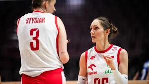 Dwie siatkarki reprezentacji Polski w białych koszulkach z czerwonymi elementami, przygotowujące się do akcji podczas meczu, skupione na rozmowie i współpracy na boisku.