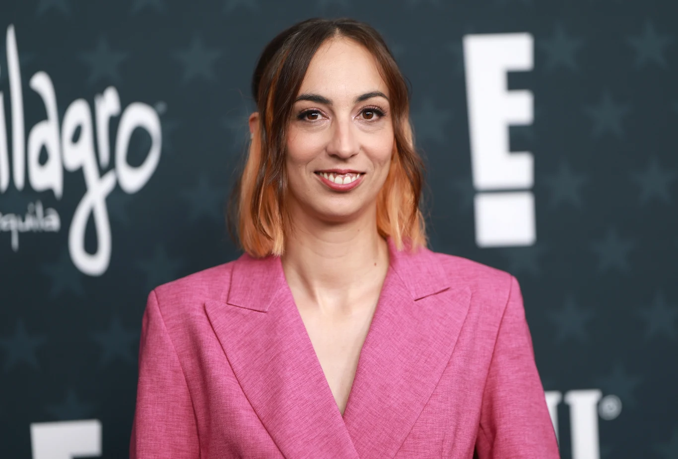 Laia Casanovas w 2026 roku Laia Casanovas w różowej marynarce, z brązowo-różowym ombre, na tle ściany z logo „E!” i gwiazdkami, 2026 rok.