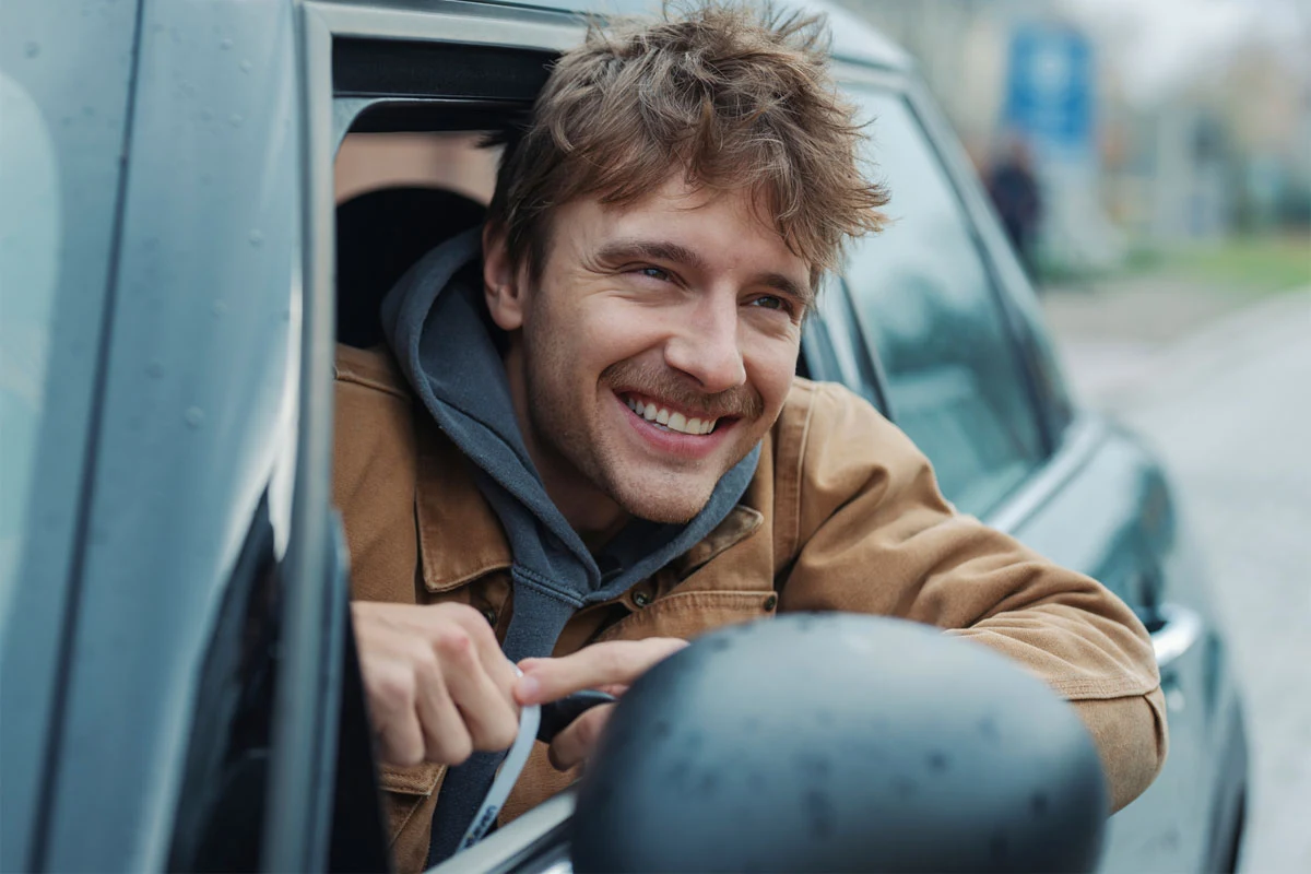 Maciej Musiał znów wciela się w Bastiana Strzygonia Maciej Musiał jako Bastian Strzygoń wygląda przez otwarte okno samochodu, opierając ręce o drzwi.