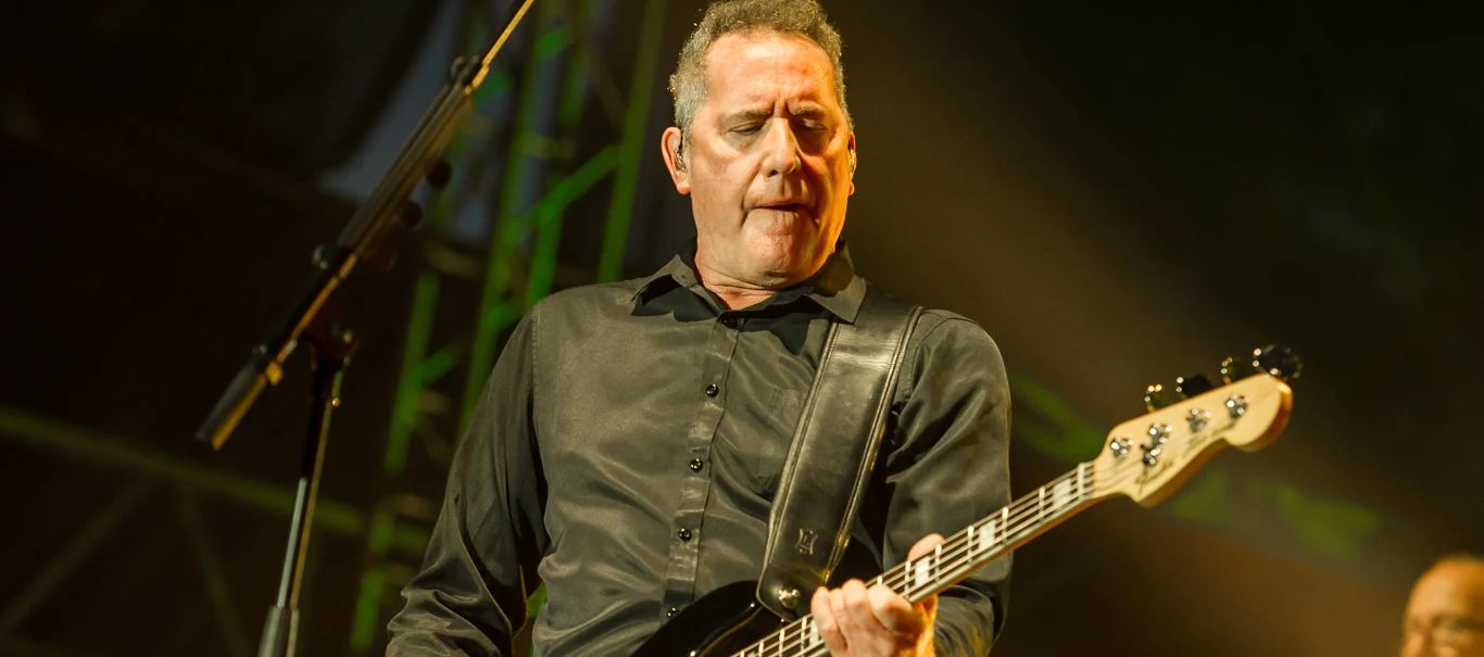 OMD w Warszawie 2026 OMD w Warszawie 2026. Mężczyzna w czarnej koszuli gra na gitarze basowej na scenie, w tle reflektory i mikrofon.