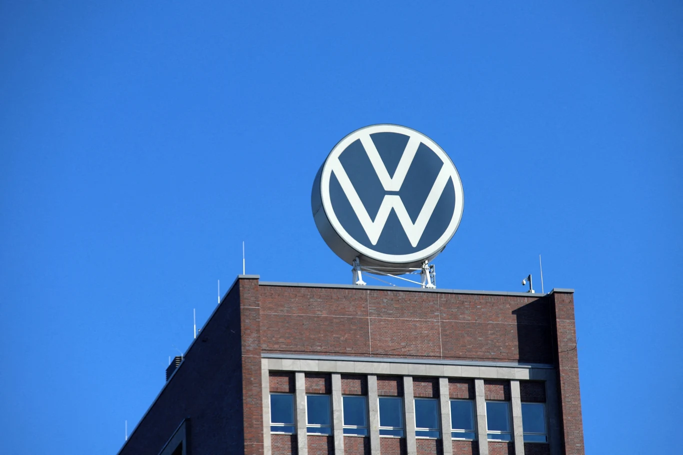 Szefowie Volkswagena tłumaczą załodze konieczność restrukturyzacji firmy. Zdj. ilustracyjne Duże logo Volkswagena na dachu ceglanego budynku na tle niebieskiego nieba