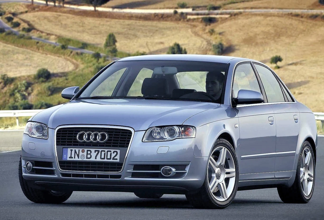 Audi A4 to jedno z pięciu najpopularniejszych używanych aut w Polsce. Statystycznie ma 20 lat i 302 tys. km przebiegu Srebrne Audi A4 stoi zaparkowane na asfaltowej drodze, na tle pagórkowatego, wysuszonego krajobrazu.