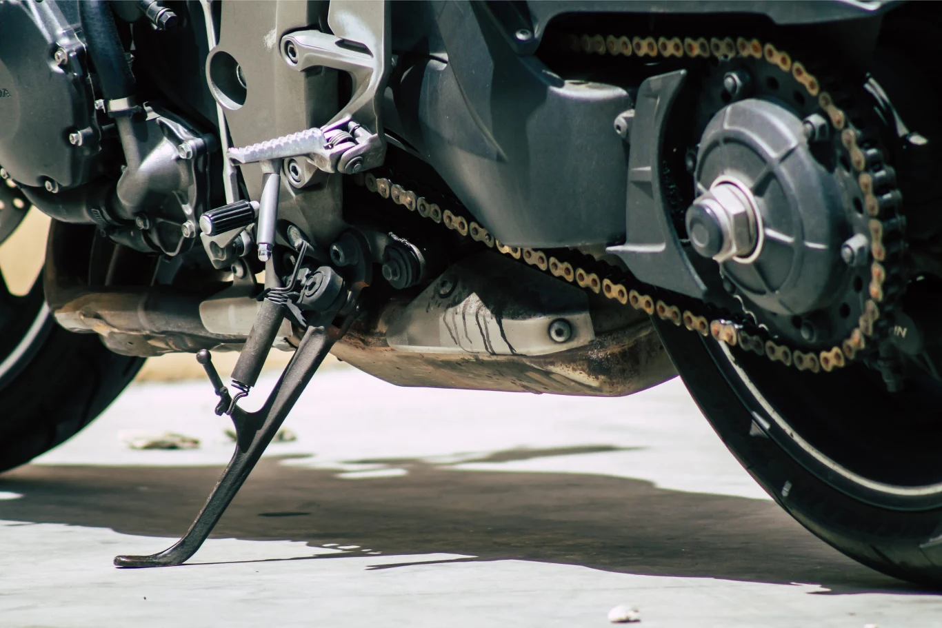 Motocykl oparty na bocznej stopce, z wyraźnie widocznym łańcuchem napędowym oraz elementami układu napędowego i wydechowego.