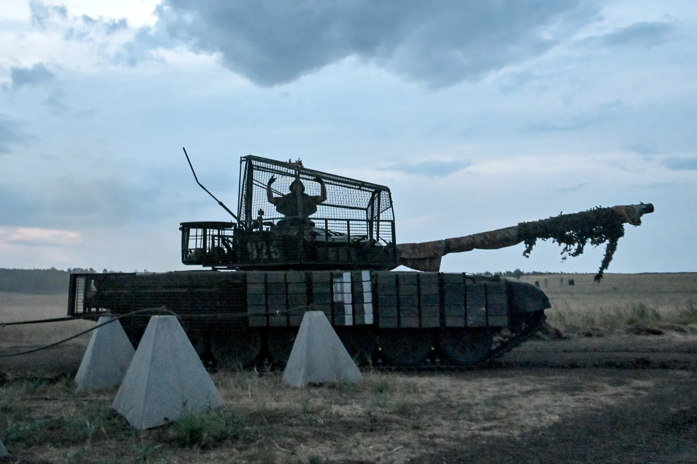 Ukraiński czołg T-72 podczas ćwiczeń zołg T-72 z osłoną przeciw dronom, na którego wieży stoi ukraiński żołnierz.