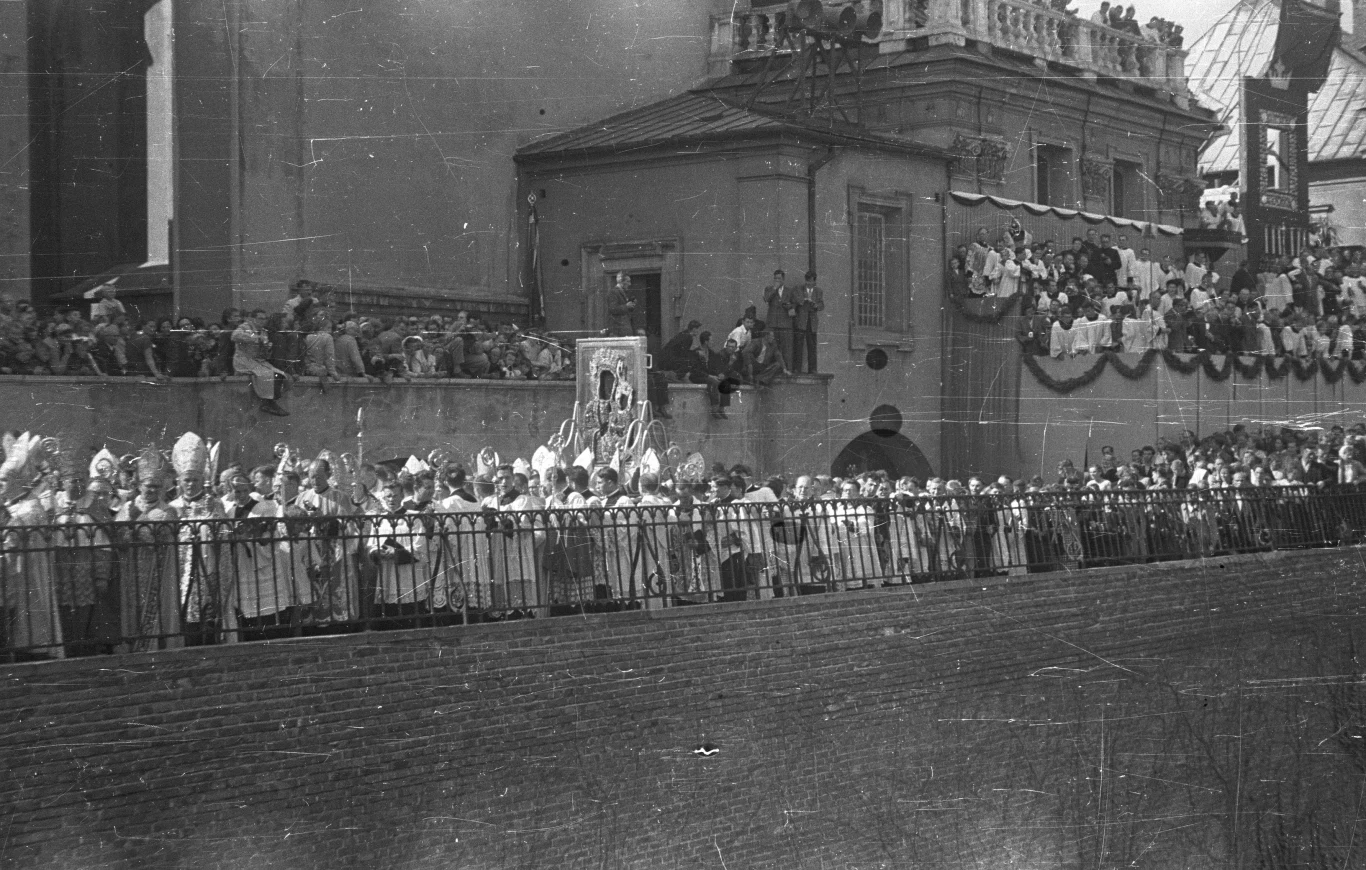 Wizerunek Matki Boskiej Częstochowskiej na murach klasztoru 26.08.1956 r. Procesja dzieci w uroczystych strojach komunijnych niosących religijne symbole, zgromadzeni wierni na schodach i balkonie udekorowanym girlandami oraz obrazem Matki Bożej.