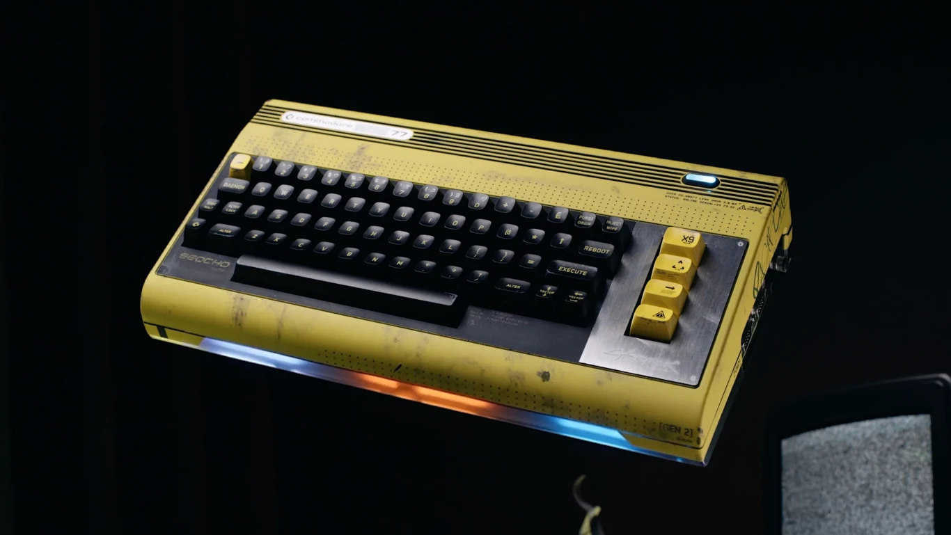 Commodore 77 Stary żółty komputer z widocznymi śladami zużycia i wyeksponowaną klawiaturą z dużymi żółtymi przyciskami po prawej stronie, unoszący się w ciemnej przestrzeni.