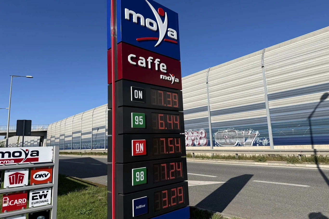 Ceny paliw na stacji Moya. Tablica cenowa stacji paliw Moya z aktualnymi cenami poszczególnych rodzajów paliwa, ustawiona przy ulicy obok ekranu akustycznego.