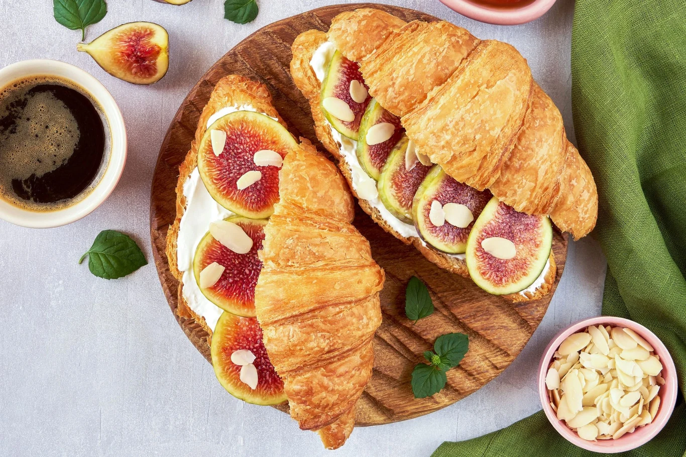 Rogaliki z figami na słodko, to jedno z moich ulubionych śniadań Dwa croissanty z kremowym serkiem, świeżymi figami i płatkami migdałów na drewnianej desce, obok kawa.