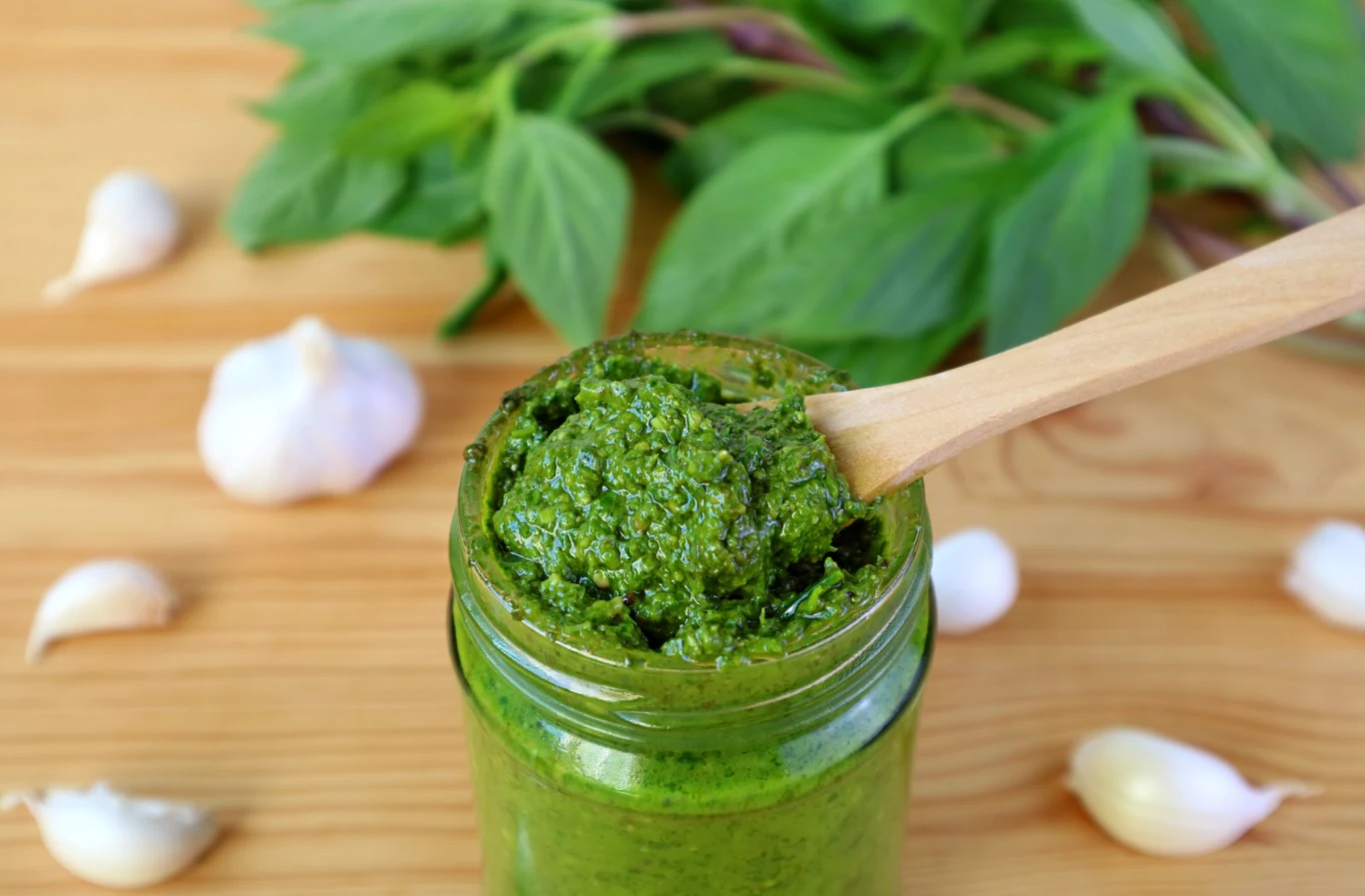 Jak zrobić pyszne domowe pesto? Słoik z pesto na drewnianym blacie.