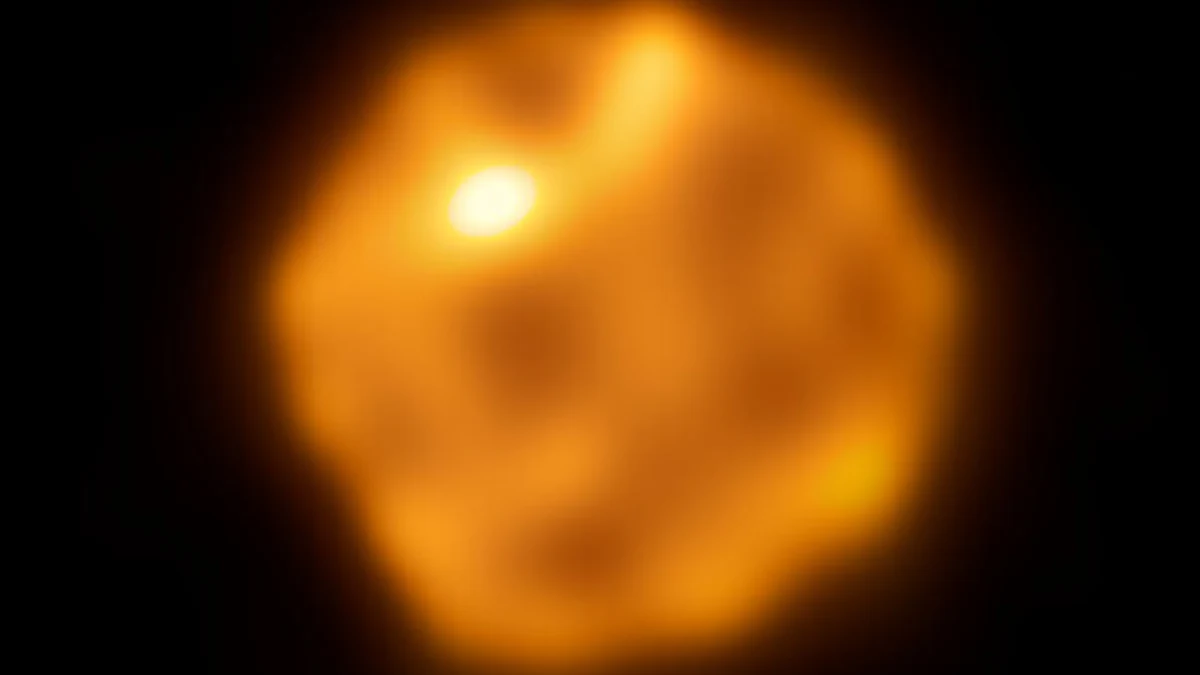 Pofałdowana powierzchnia gwiazdy Betelgeza na zdjęciu z ALMA. Jasna, rozmyta kula o nieregularnych kształtach i intensywnym pomarańczowo-żółtym świetle, otoczona ciemnym tłem.