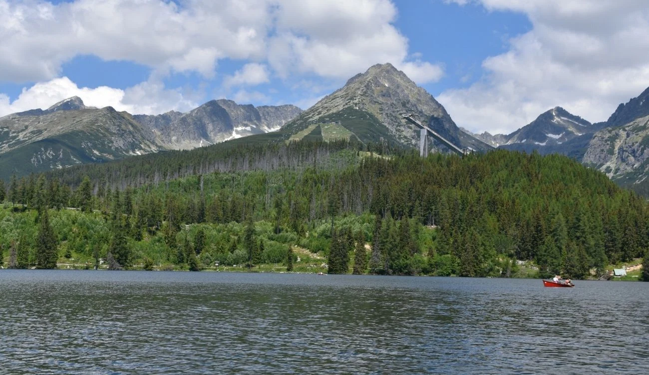 Szczyrbskie Jezioro w Tatrach Wysokich leży na wysokości 1346 m n.p.m. Szczyrbskie Jezioro w otoczeniu lasu i gór, widoczna skocznia narciarska oraz czółno na wodzie.