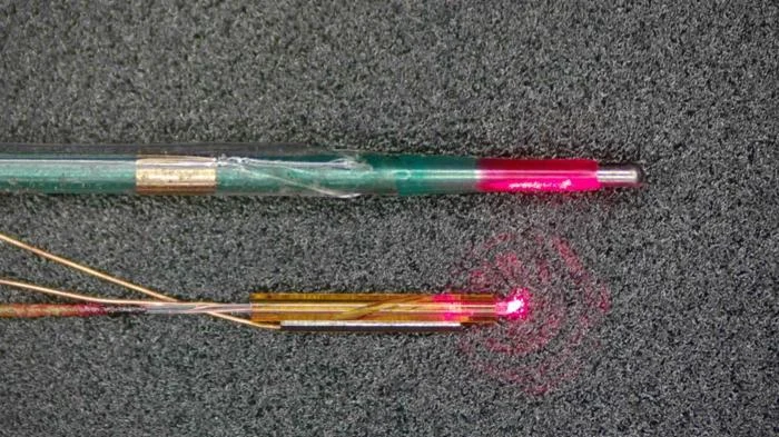 Dwa urządzenia medyczne z cienkimi przewodami, z których dolne emituje czerwone światło laserowe skupione w jednym punkcie.