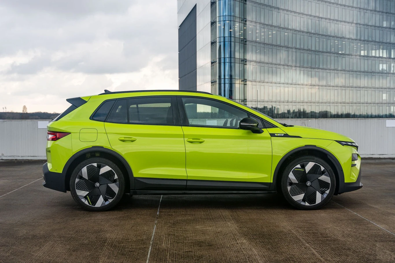 Skoda Elroq ma 4,48 m długości. Jaskrawozielony, nowoczesny SUV o dynamicznej sylwetce, charakterystycznych felgach oraz mocno zarysowanych liniach nadwozia, zaparkowany na betonowej nawierzchni przy szklanym budynku.