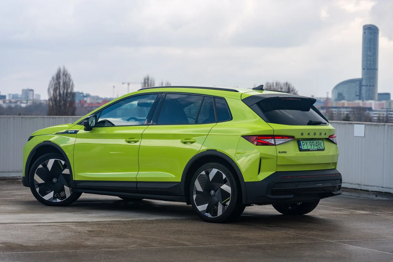 Skoda Elroq generuje 340 KM i rozpędza się do setki w 5,4 s. Jaskrawozielony samochód Skoda Enyaq Coupe stojący na parkingu, widoczny z tyłu i z boku, z charakterystycznymi czarnymi felgami i przyciemnianymi szybami.