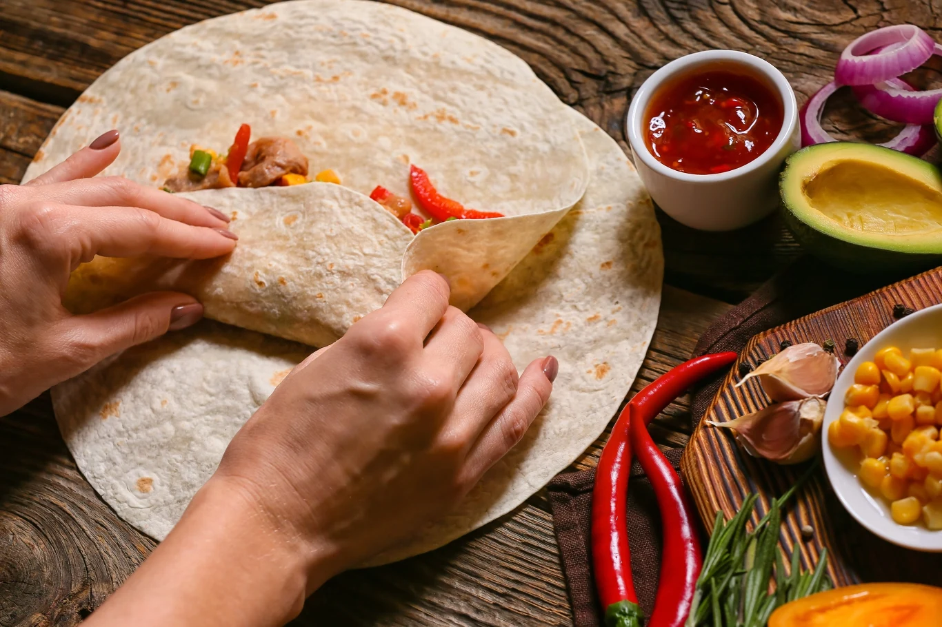 Co zrobić na szybki obiad po szkole? Przygotowaliśmy 5 prostych przepisów Tortilla z warzywnym farszem, na stole awokado, papryka, cebula, chili, kukurydza i salsa.