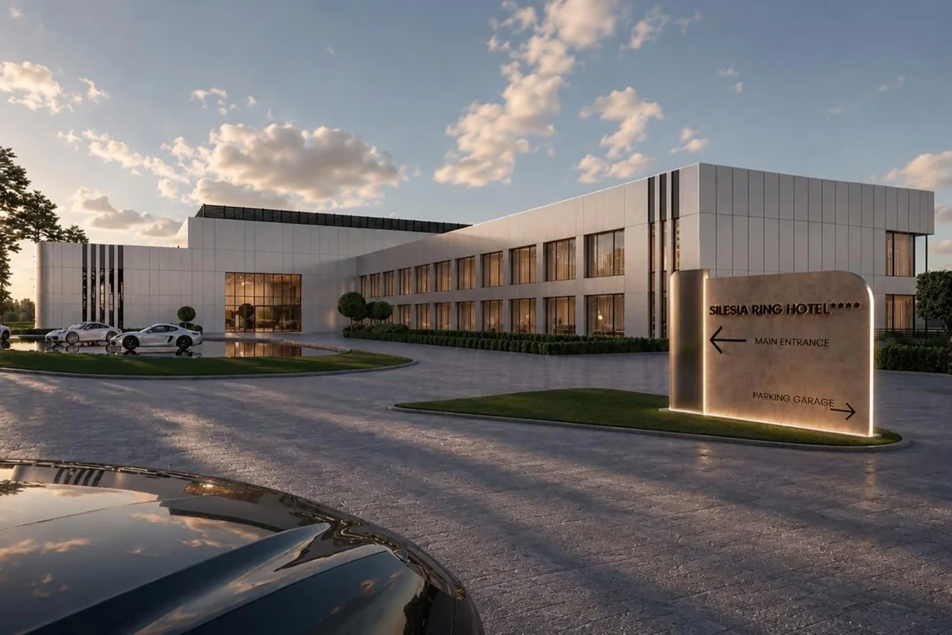 Budowa nowego hotelu ma zakończyć się w 2028 roku | Fot. Newsroom Silesia Ring Nowoczesny budynek hotelu z prostą, elegancką bryłą oraz jasną elewacją, przed którym stoi podświetlony kierunkowskaz i zaparkowane samochody.