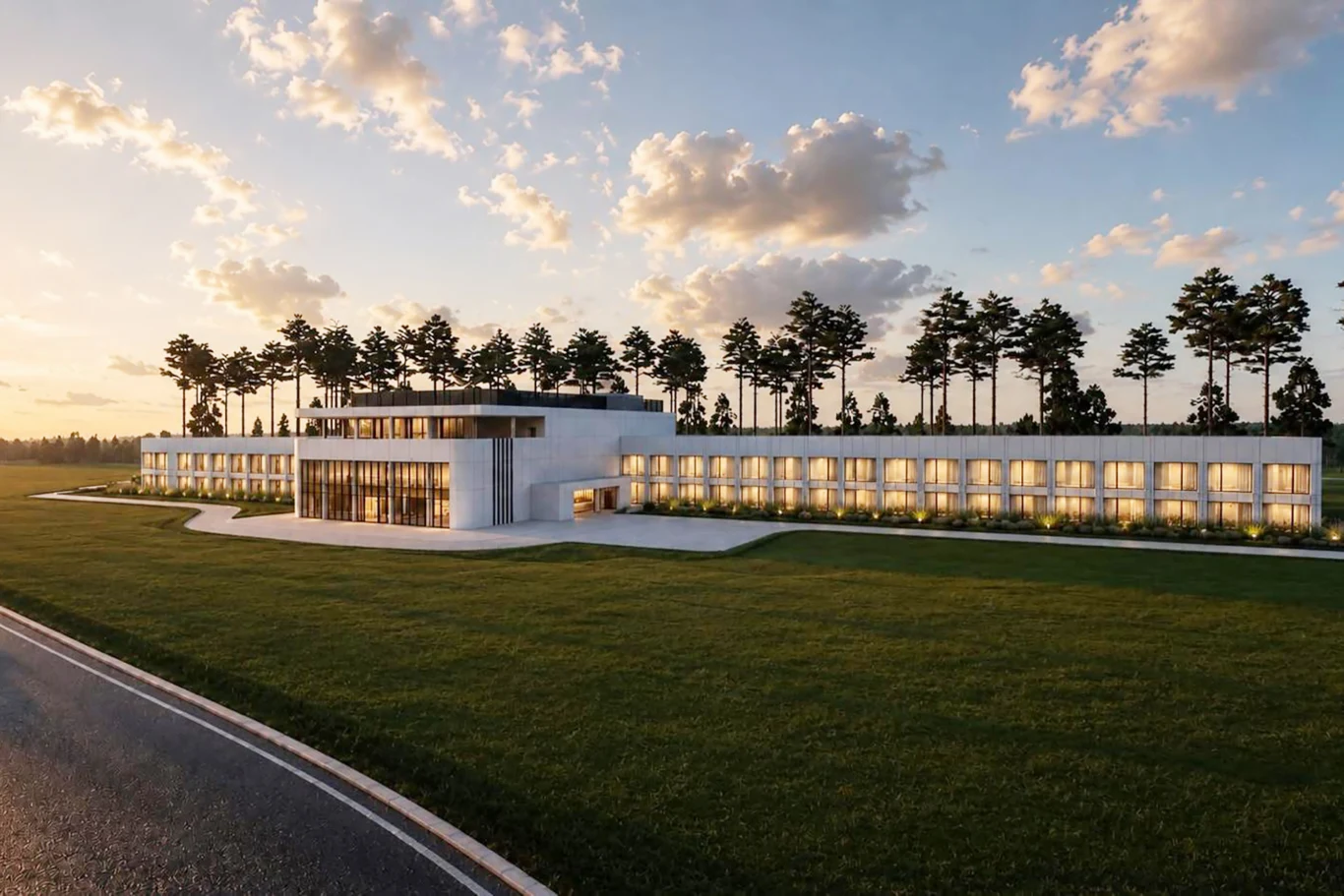 Wizualizacja hotelu Silesia Ring w Kamieniu Śląskim | Fot. Newsroom Silesia Ring Nowoczesny, rozległy budynek z dużymi przeszkleniami i podświetleniem, otoczony zielonym trawnikiem, z linią wysokich drzew rosnących w tle na tle nieba o zachodzie słońca.