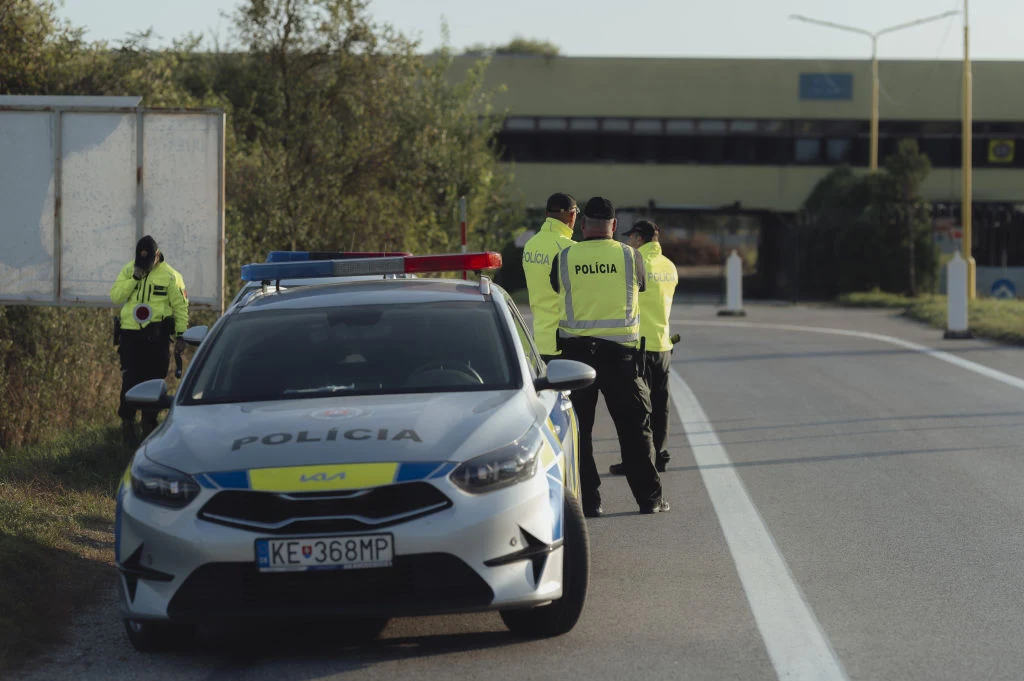 Słowacka policja udaremniła atak na fabrykę dronów (zdj. ilustracyjne) Radiowóz słowackiej policji przy drodze, kilku policjantów w żółtych kamizelkach rozmawia obok pojazdu.