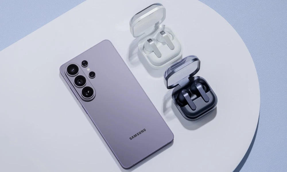 Samsung Galaxy S26 Ultra i słuchawki Galaxy Buds4 Fioletowy smartfon Samsung leży obok dwóch etui z bezprzewodowymi słuchawkami w kolorze białym i czarnym, ułożonych na jasnej, minimalistycznej powierzchni.