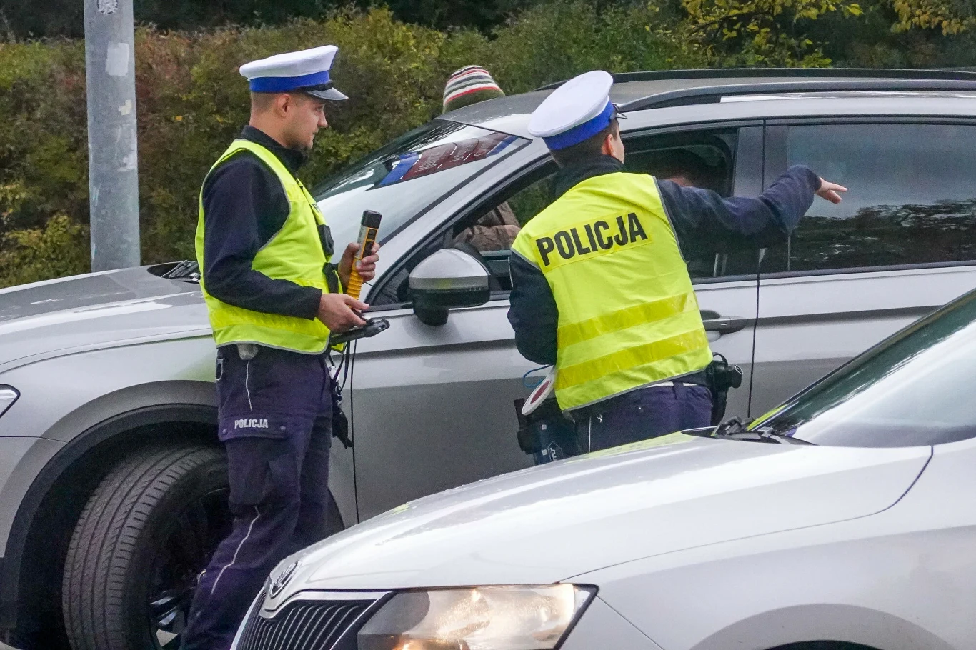 Nie masz pieniędzy na mandat? Jest prosty patent na raty Dwóch policjantów w odblaskowych kamizelkach kontroluje kierowcę w srebrnym aucie, jeden używa alkomatu