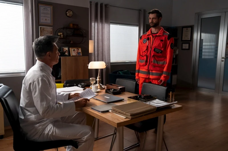 Do obsady serialu dołączył Tomasz Osica. Aktor wcieli się w Darka Babińskiego Lekarz w białym kitlu rozmawia z ratownikiem medycznym w czerwonym kombinezonie przy biurku w gabinecie.