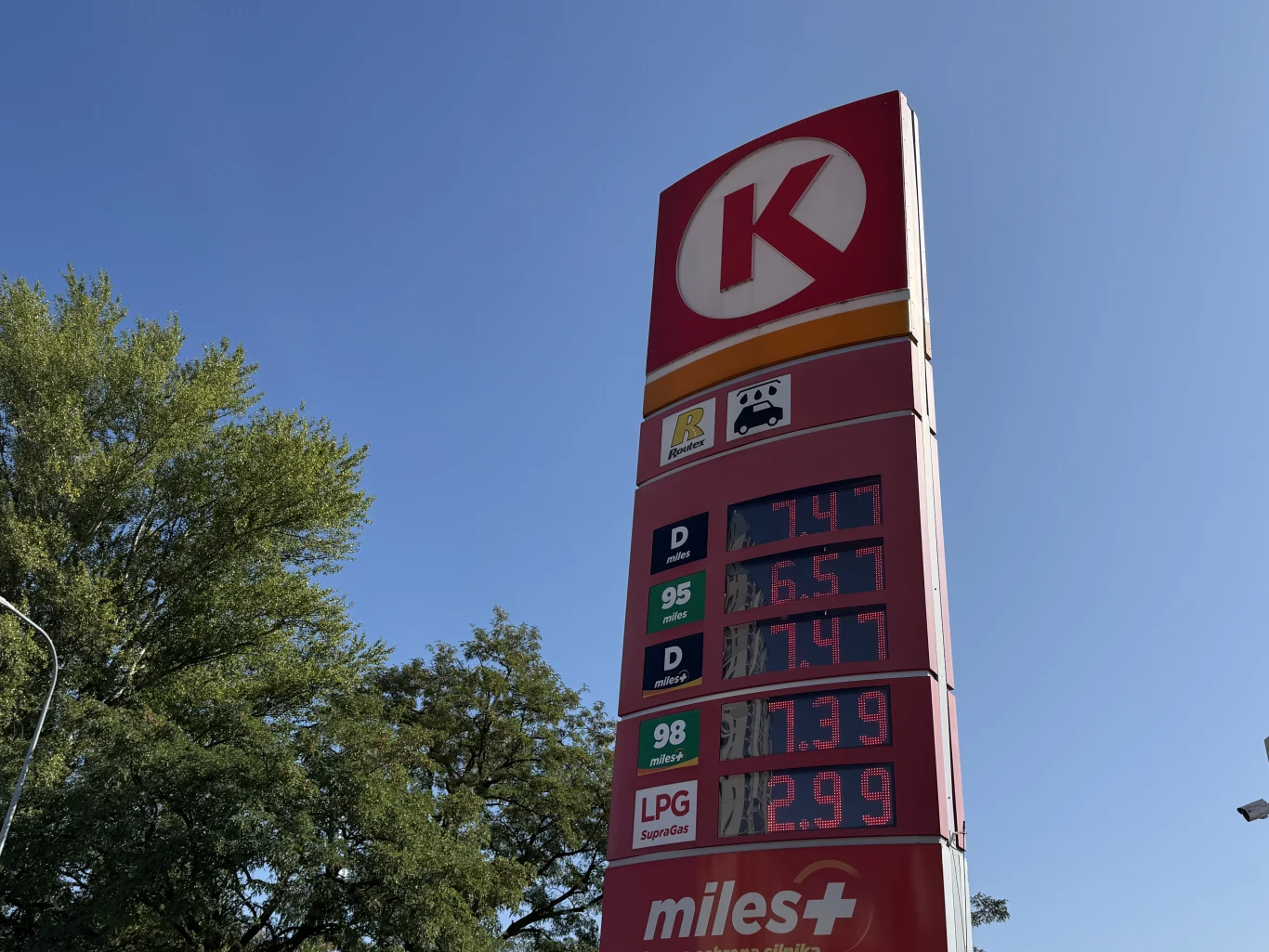 Ceny paliw na Circle K 27 sierpnia Czerwony pylon stacji paliw Circle K z wyraźnie widocznymi aktualnymi cenami paliw i niebieskim niebem w tle.