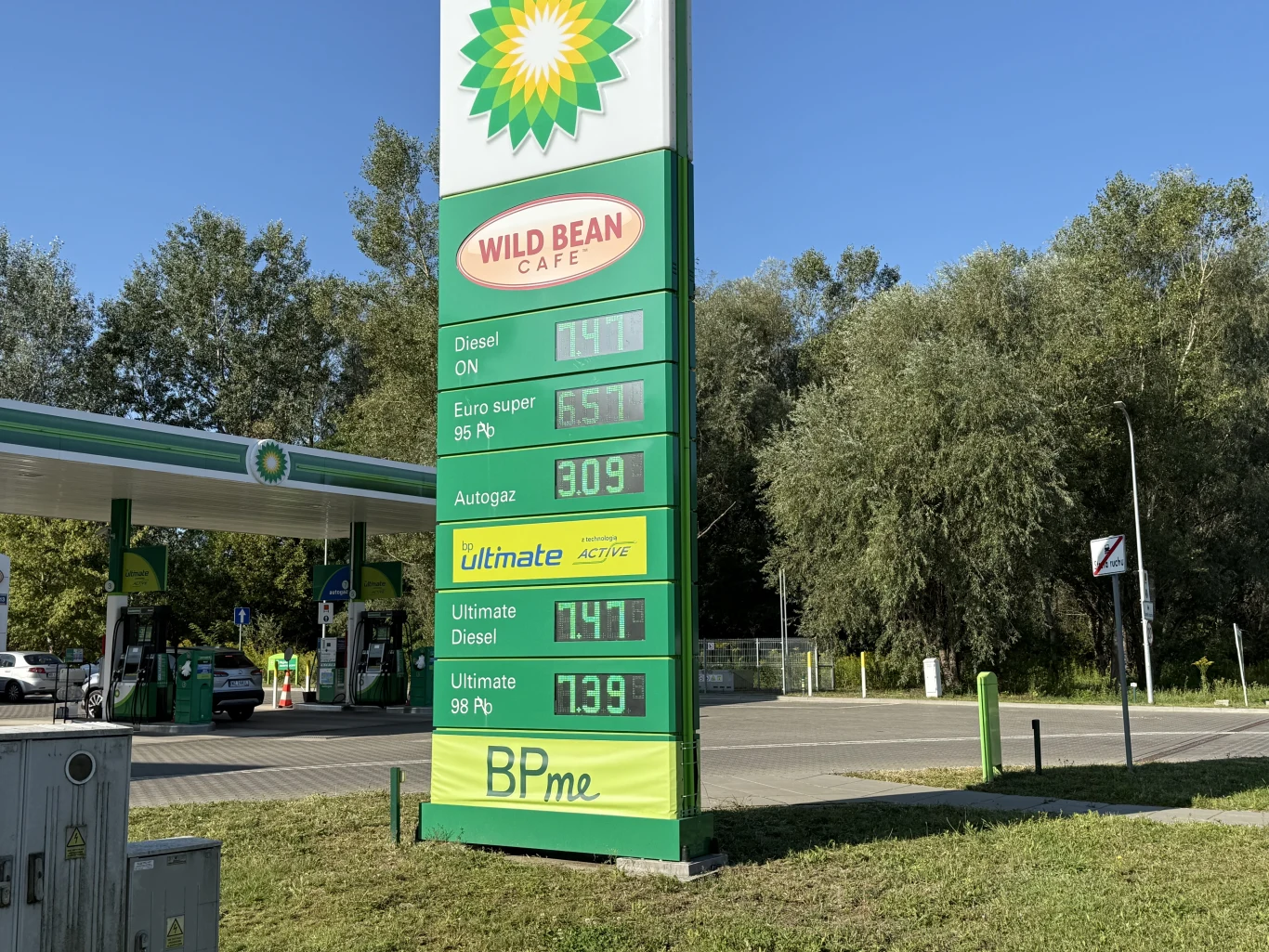 Ceny paliw na BP 27 sierpnia Pylon stacji BP z aktualnymi cenami paliw oraz widocznym logo, w tle fragment dystrybutorów i zadaszenie stacji otoczone zielenią.