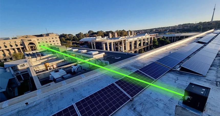 Koniec problemów z zakłóceniami? Naukowcy przesłali dane laserem przez silne turbulencje Zielony promień lasera przesyłany między dachami budynków z widoczną instalacją paneli słonecznych.