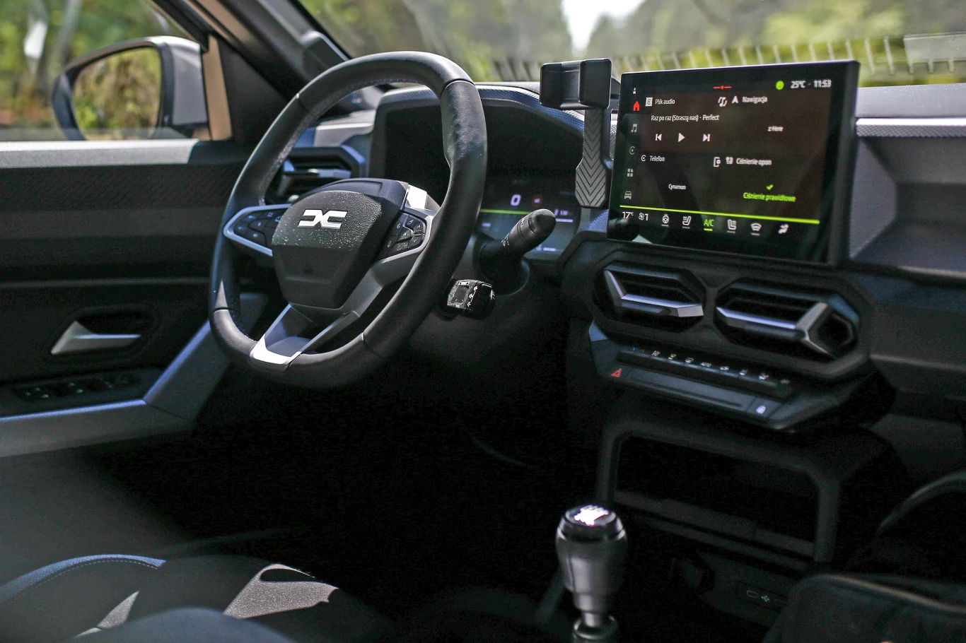 Kierownica z logo marki Dacia, nowoczesny ekran dotykowy wyświetlający system multimedialny oraz charakterystyczne, sześciokątne nawiewy w centralnej części deski rozdzielczej.