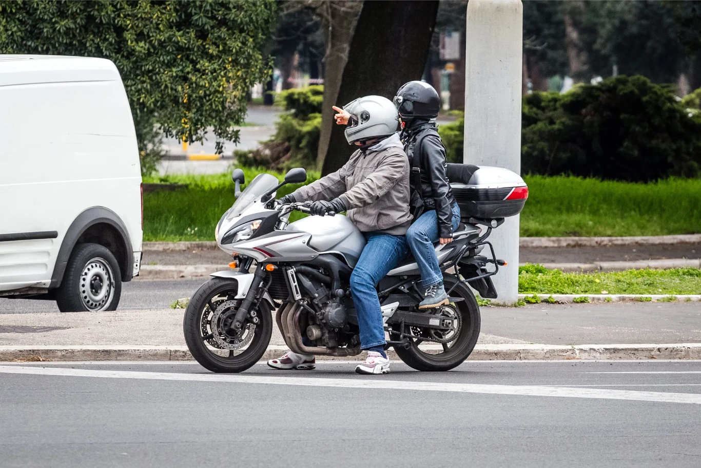 Czy w Polsce można jeździć na motocyklu z dzieckiem? Dwóch motocyklistów w kaskach na srebrnym motocyklu, jeden wskazuje kierunek ręką
