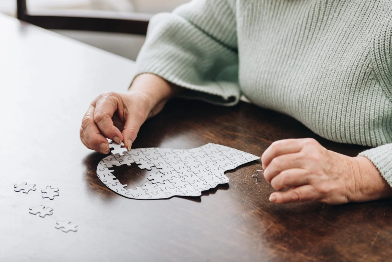 Po pięćdziesiątce w mózgu może rozpoczynać się cicha przebudowa Starsza osoba układa puzzle w kształcie ludzkiej głowy na drewnianym stole.