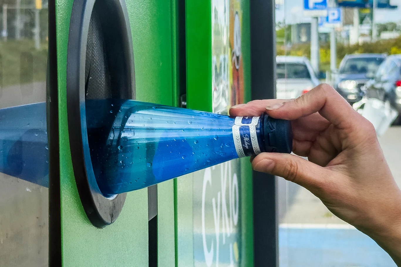 Aby butelkomat nie odprawił nas z kwitkiem, butelkę można najpierw sprawdzić w internecie Ręka wkładająca pustą plastikową butelkę do zielonego automatu do recyklingu.