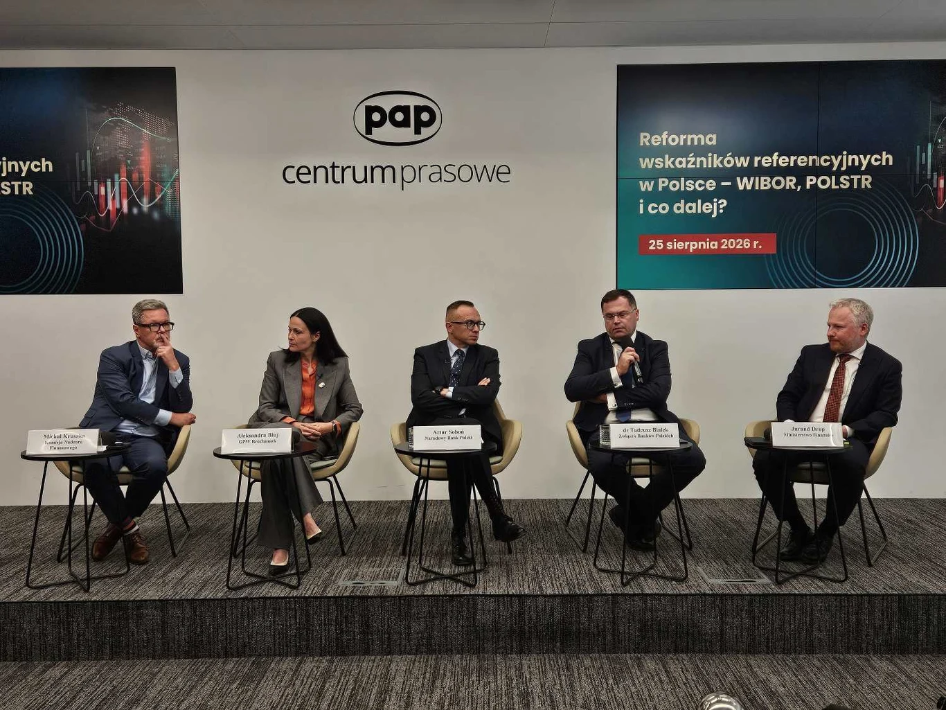Pięcioro prelegentów siedzących na scenie podczas konferencji prasowej PAP, rozmawiających o reformie wskaźników referencyjnych w Polsce; każdy z nich ma przed sobą tabliczkę z imieniem i nazwiskiem, a w tle widoczne są logotyp oraz tytuł wydarzenia.