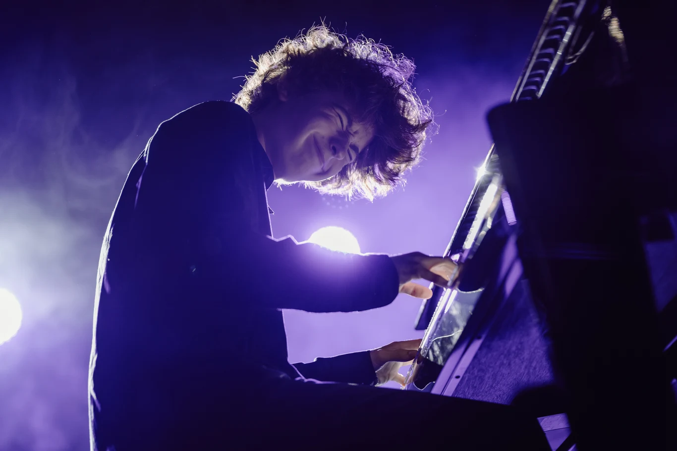 Kuba Derej Pianista z energią gra na fortepianie, otoczony fioletowym światłem sceny i skupiony na muzyce.