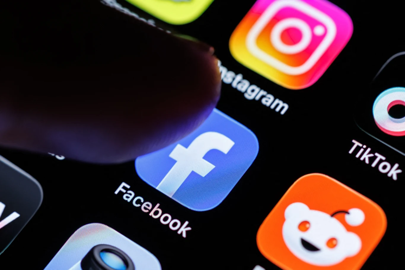 Ograniczenia social media dla nieletnich. KE wzywa Metę po sprawie w USA Ekran smartfona z ikonami Facebooka, Instagrama, TikToka i Reddit; palec dotyka ikonę Facebooka.