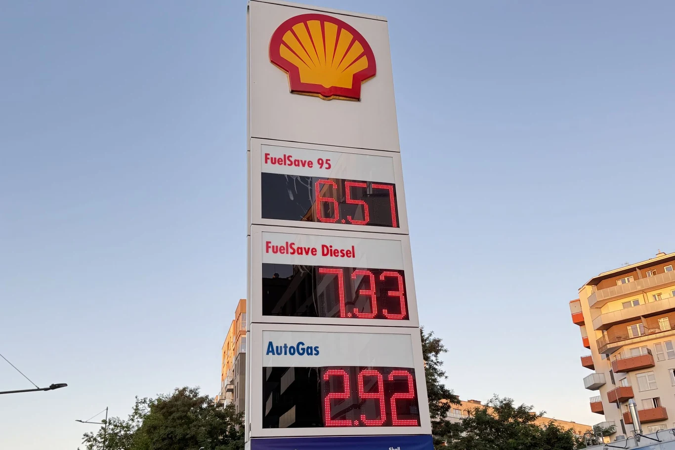 wysoki pylon stacji Shell z dużym, żółto-czerwonym logo i cyfrowym wyświetlaczem aktualnych cen paliw: benzyna 6.57, diesel 7.33, autogaz 2.92