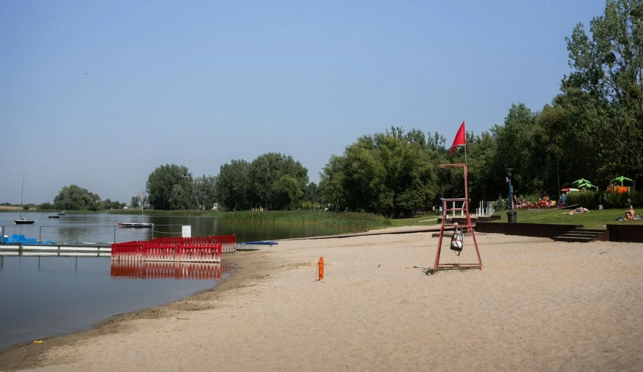 Jezioro Średzkie wysycha, a cofająca się linia brzegowa odsłania dno Jezioro Średzkie z cofającą się linią brzegową, piaszczysta plaża, wieża ratownika, czerwona flaga, parasole.