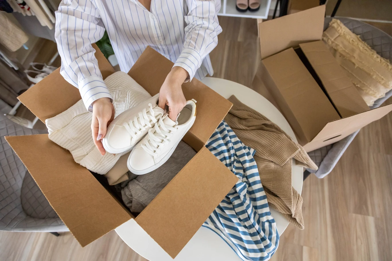 Twoje nowe buty się zepsuły? Do reklamacji nie potrzebujesz oryginalnego pudełka, Osoba trzymające białe sneakersy nad kartonem z ubraniami.
