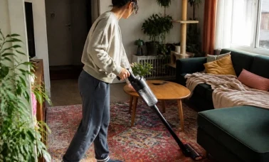 Bezprzewodowy odkurzacz pionowy czyści drewnianą podłogę przy wzorzystym dywanie 