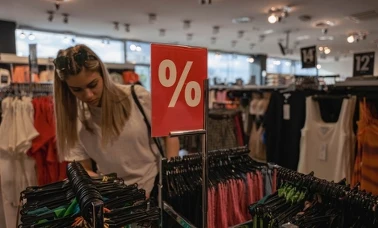  Klientka przegląda ubrania na wieszakach obok czerwonej tabliczki z symbolem procentu 