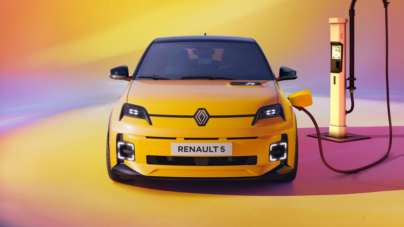 Żółty samochód Renault 5 ustawiony naprzeciwko stacji ładowania, podłączony do ładowarki elektrycznej na tle kolorowych, abstrakcyjnych gradientów.