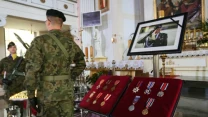 Żołnierze w mundurach stoją obok ekspozycji z odznaczeniami wojskowymi i zdjęciem wojskowego, ustawionej w kościele przy ołtarzu.