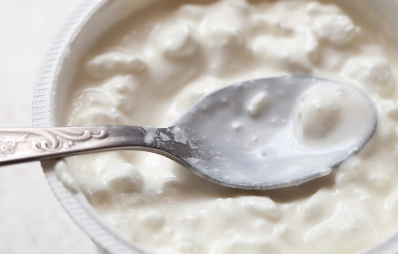 Zdaniem naukowców, spośród produktów mlecznych najbardziej korzystne są dla ludzi te fermentowane - np. kefir Srebrna łyżka w twarożku ziarnistym w białym plastikowym pojemniku, przykład produktu mlecznego.