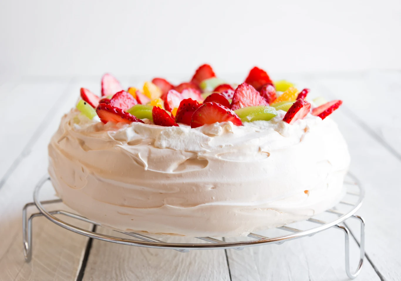 Jak piec bezę? Tort bezowy z warstwą kremu, ozdobiony truskawkami i kiwi.