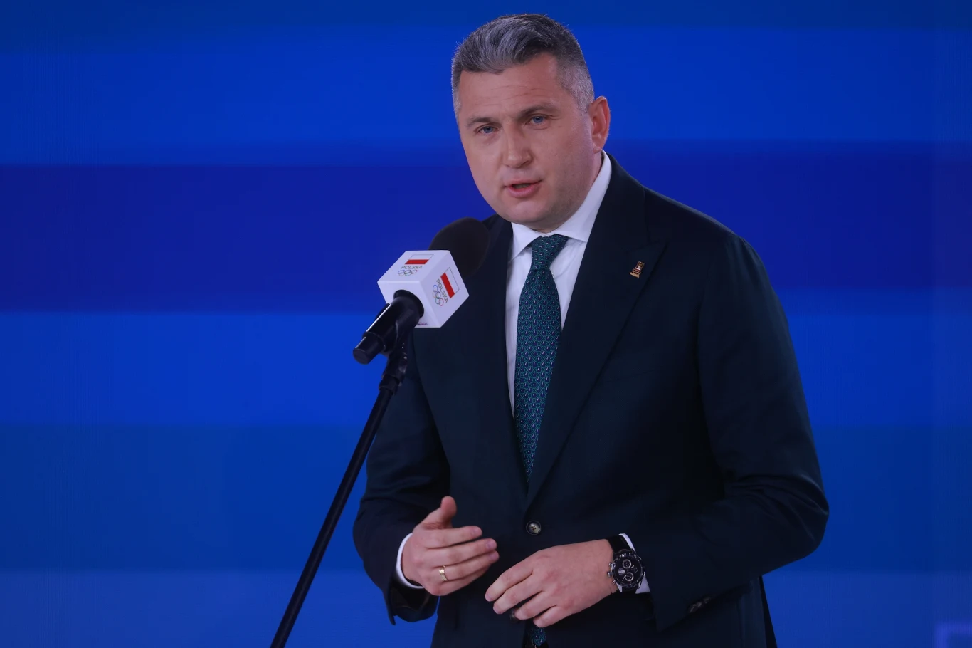 Sąd zdecydował o areszcie tymczasowym dla Radosława Piesiewicza Radosław Piesiewicz w garniturze i zielonym krawacie przemawia do mikrofonu na tle niebieskiej sceny.