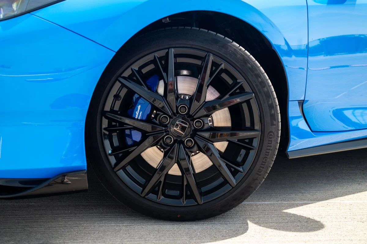 19-calowe obręcze i hamulce Brembo nie wymagają dopłaty. Czarna felga aluminiowa z widocznym logo Honda, niebieski zacisk hamulcowy i przedni błotnik sportowego samochodu w kolorze niebieskim.