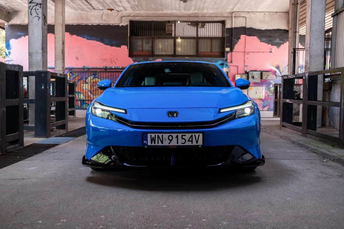 Z przodu Prelude bardziej przypomina modele Toyoty niż Hondy. Jasnoniebieski samochód osobowy Honda Civic ustawiony przodem na środku opustoszałej, industrialnej przestrzeni, w tle kolorowy mural na ścianie.