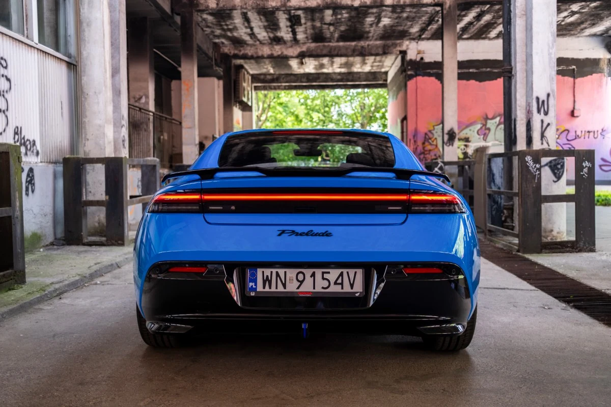 Efektowny czerwony pas świetlny dodaje charakteru. Tył niebieskiego samochodu sportowego Honda Prelude z charakterystycznym pasem świetlnym, widoczną nazwą modelu i tablicą rejestracyjną na tle betonowego parkingu z kolorowymi graffiti.